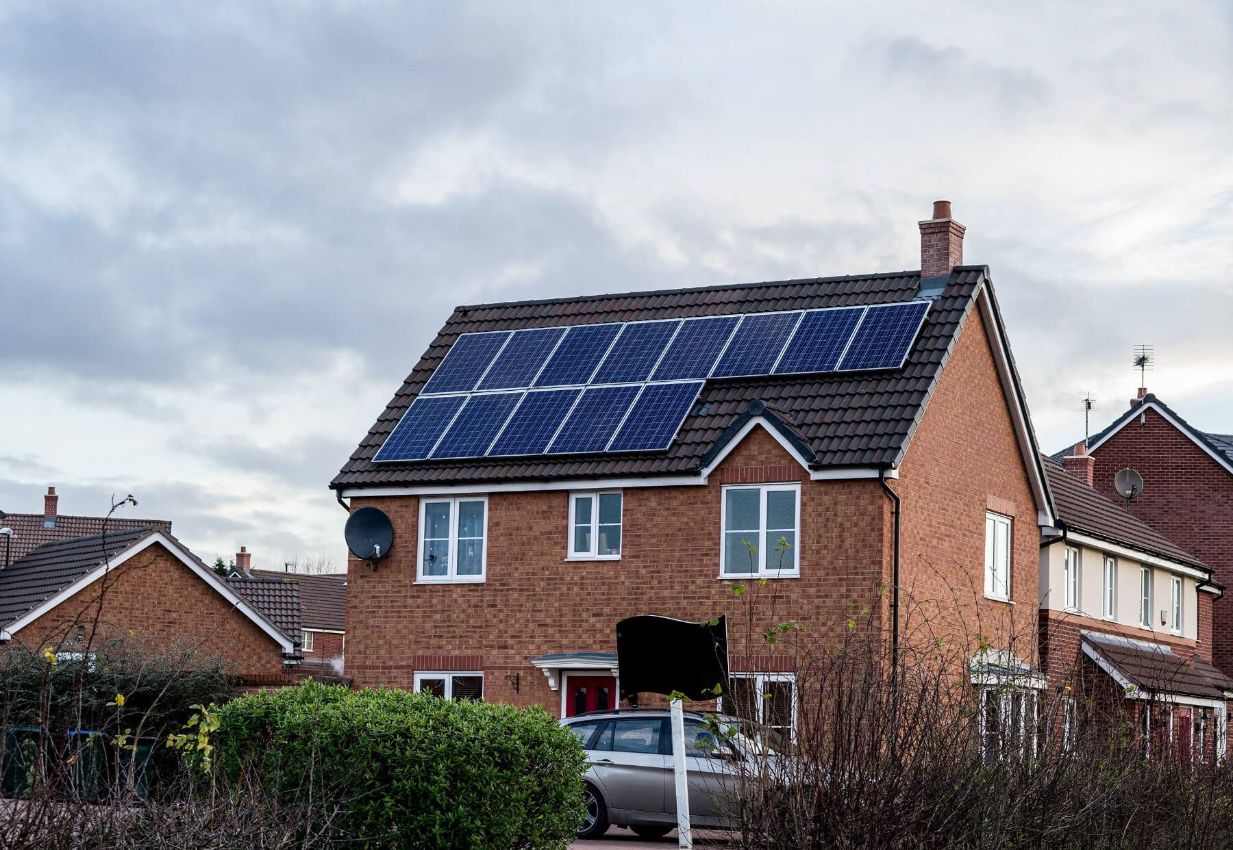 a house with solar panels on the roof and hedge in front of it